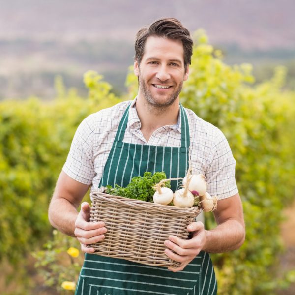 Young happy farmer holding a basket of vegetables in the field